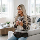 Woman wearing the URBAN SAFARI TOP with leopard print and color block design, holding a mug indoors.