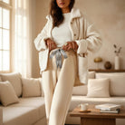 Woman wearing COMFORT CULTURE PANTS (cream) with leopard drawstring, cozy fleece interior, stylish living room setting.