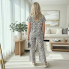 Back view of a woman wearing the WILD GRACE 2 PC PANTS SET in a trendy leopard print, styled in a chic living space.