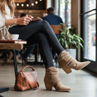 Woman wearing ARISA STRAPPY ANKLE BOOTS at a cafe, showcasing the stylish strappy design and block heel.