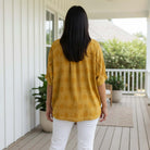 Back view of a woman wearing the DOT DIRECTIONS TOP - Umgee (gold) with polka dots, styled with white pants.