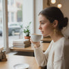 A woman wearing REFINED RIBBON EARRINGS, enjoying coffee in a cozy cafe with a modern aesthetic.