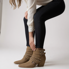 Model adjusting ARISA STRAPPY ANKLE BOOTS with studded straps and block heel, perfect for chic outfits.