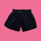 LULU MAC ACTIVE SHORTS (black) laid flat on a pink background, showcasing their lightweight and sporty design.