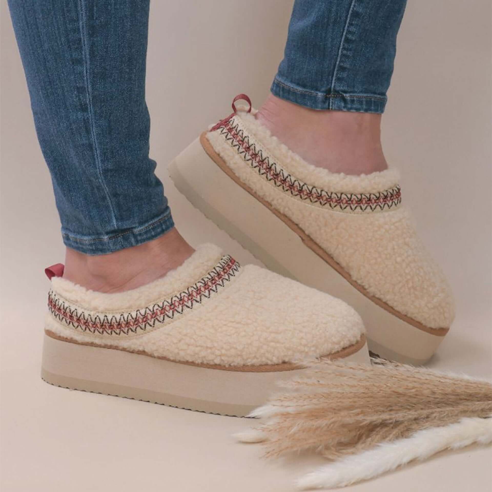 Cozy platform slippers with sherpa upper and embroidered detail, paired with jeans, offering style and comfort for all-day wear.