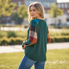 A woman wearing the HIGHLAND RETREAT TOP with plaid sleeves, standing outdoors in a sunlit setting.