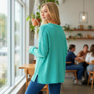 Model wearing COZY CONCEPTS RIBBED TOP (turquoise) in a café setting, showcasing its relaxed fit and soft rib knit design.